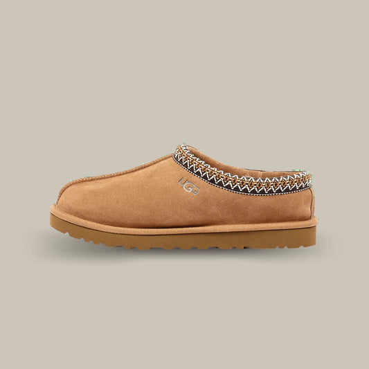 La Ugg Tasman Slipper Chestnut de coté avec sa tige en daim marron, son tressage en polyester recyclé rouge et blanc et sa semelle en EVA.