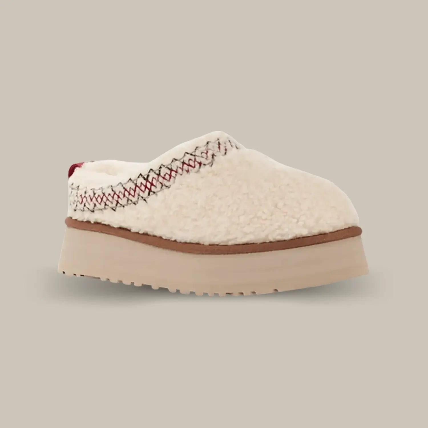 La UGG Tazz Braid Natural de coté avec sa tige en duvet beige, sa tresse rouge et noir en polyester et sa semelle compensée en EVA de 4.4 cm.